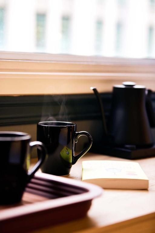 Zwarte mokken en een koffiepot op een zonnige houten tafel bij een raam.