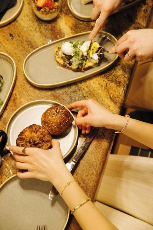 Handen die brood en salade serveren aan een restauranttafel met borden en bestek.
