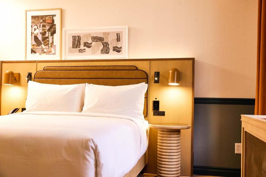 Hotelkamer met een netjes opgemaakt bed, sfeervolle nachtlampjes en ingelijste kunst boven het hoofdeinde.
