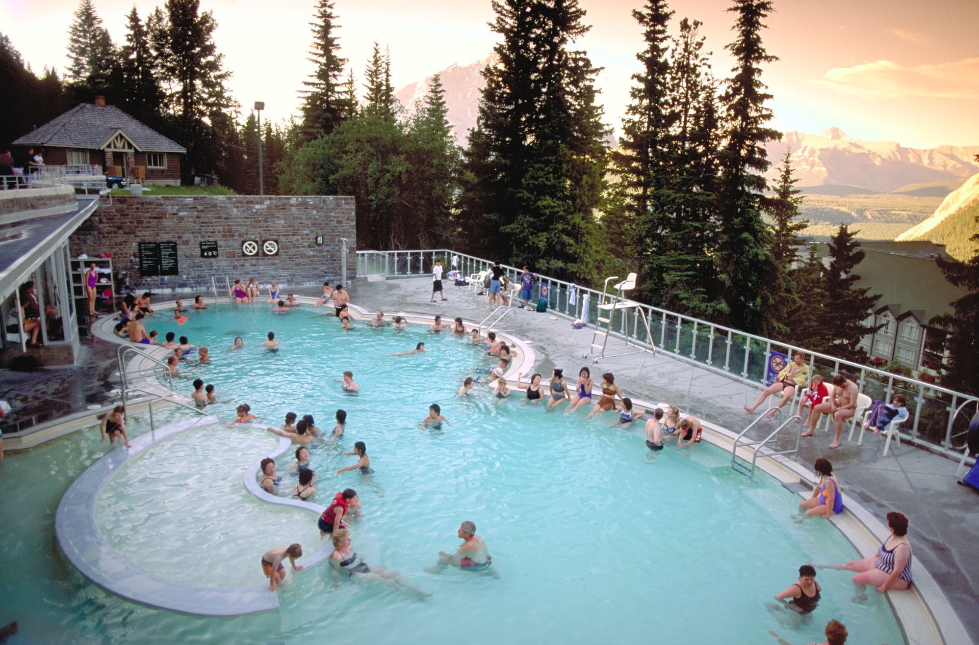 Het openluchtbad Upper Hot Springs in Banff National Park met warmwaterbronnen, gelegen naast een lodge en omgeven door pijnbomen bij zonsondergang, is drukbezocht.