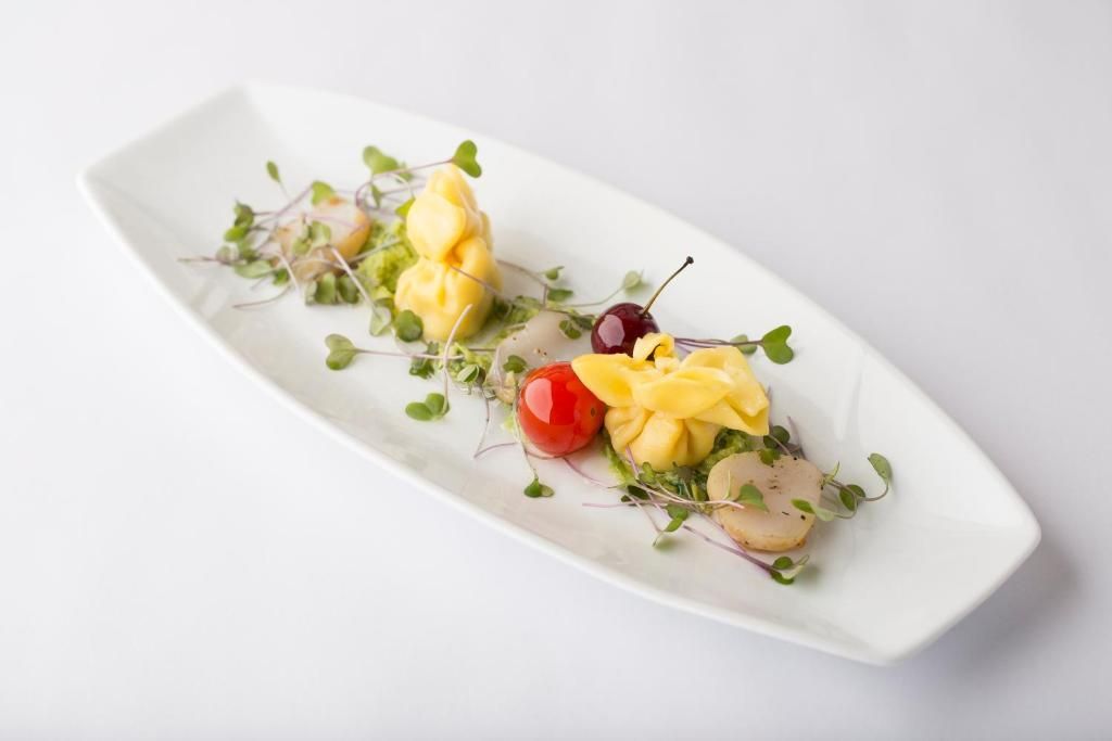 Een prachtig opgemaakte gastronomische salade met groene bladgroenten, cherrytomaten en een schepje room op een wit bord.