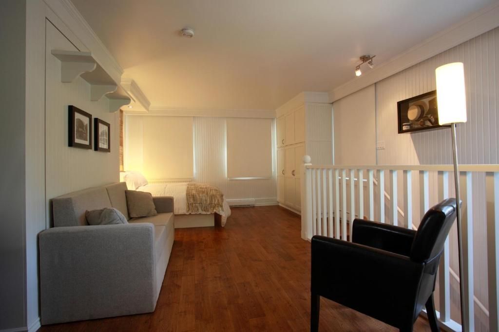 Moderne kamer van Village Historique de Val-Jalbert met grijze bank, zwarte fauteuil, houten vloer en gestreepte wanddecoratie.