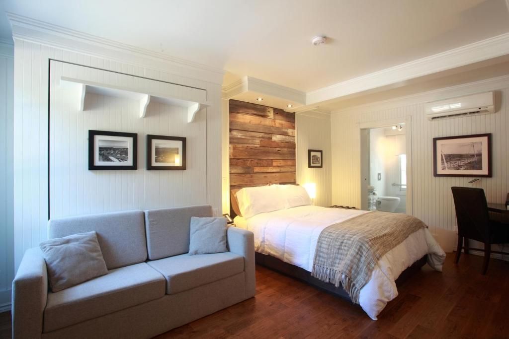 Moderne studio-slaapkamer van Village Historique de Val-Jalbert met een bed, grijze bank, bakstenen accentmuur en bureau bij het raam.