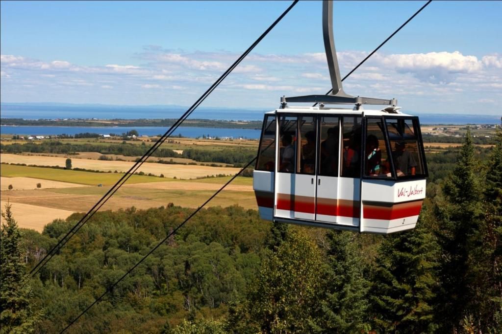 Een kabelbaanwagon hangt boven een bosrijk landschap met velden en een verre horizon.