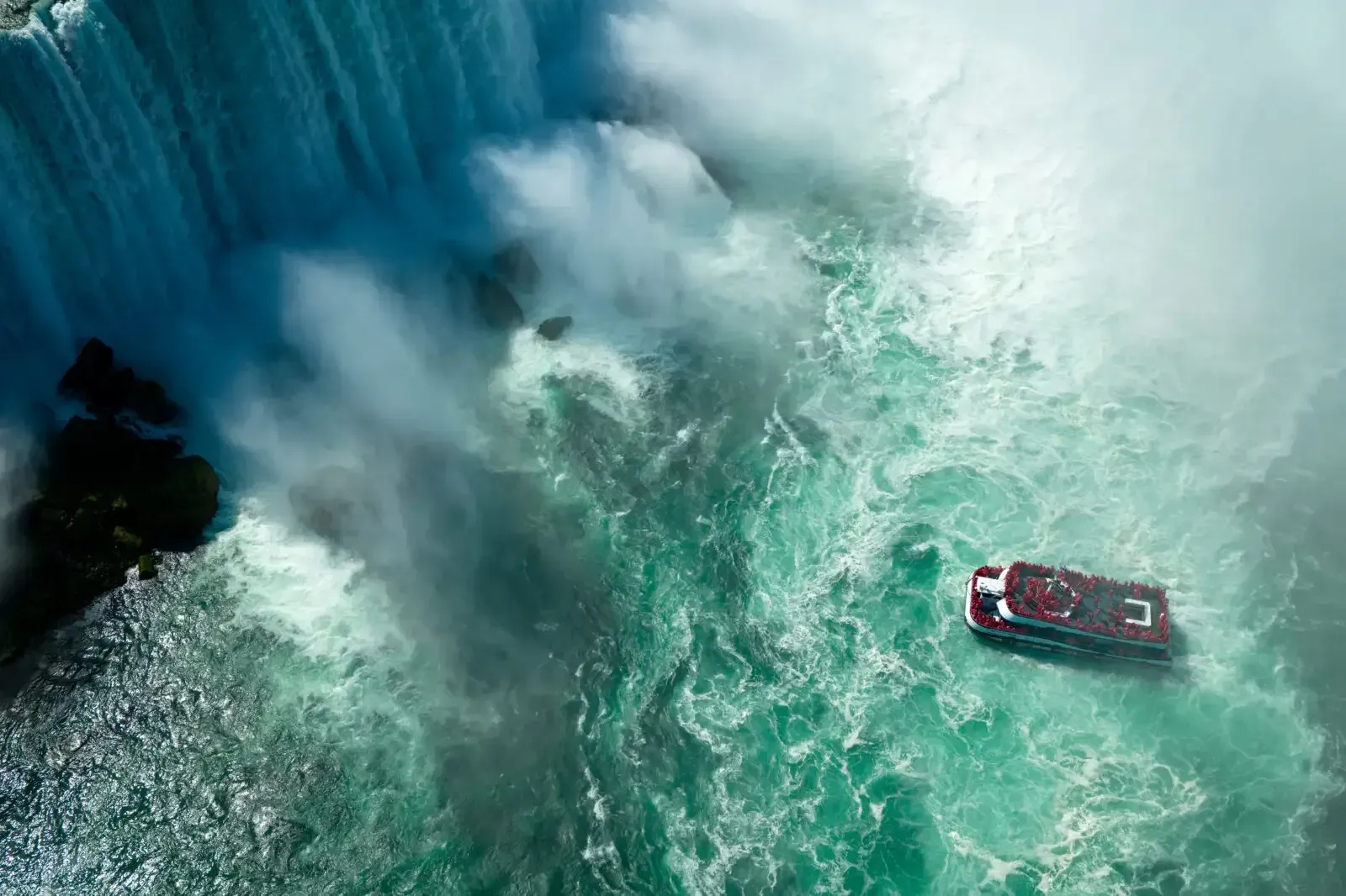 Luchtfoto van een rode boot in kolkend turquoise water nabij een krachtige waterval.