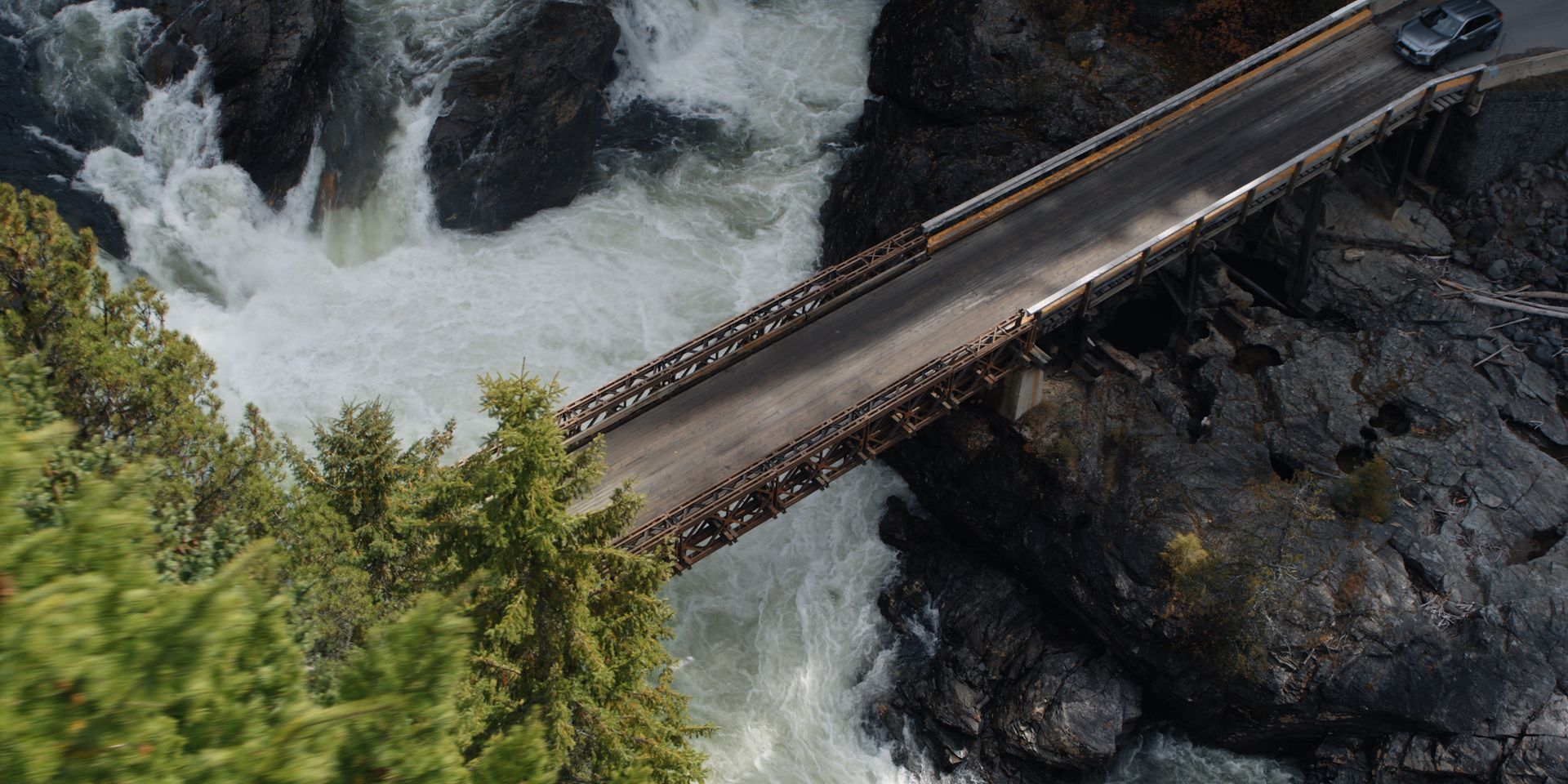 De Mushbowl Bridge in Wells Grey Provincial Park overspant een bulderende waterval naast rotsachtige kliffen en groene bomen.