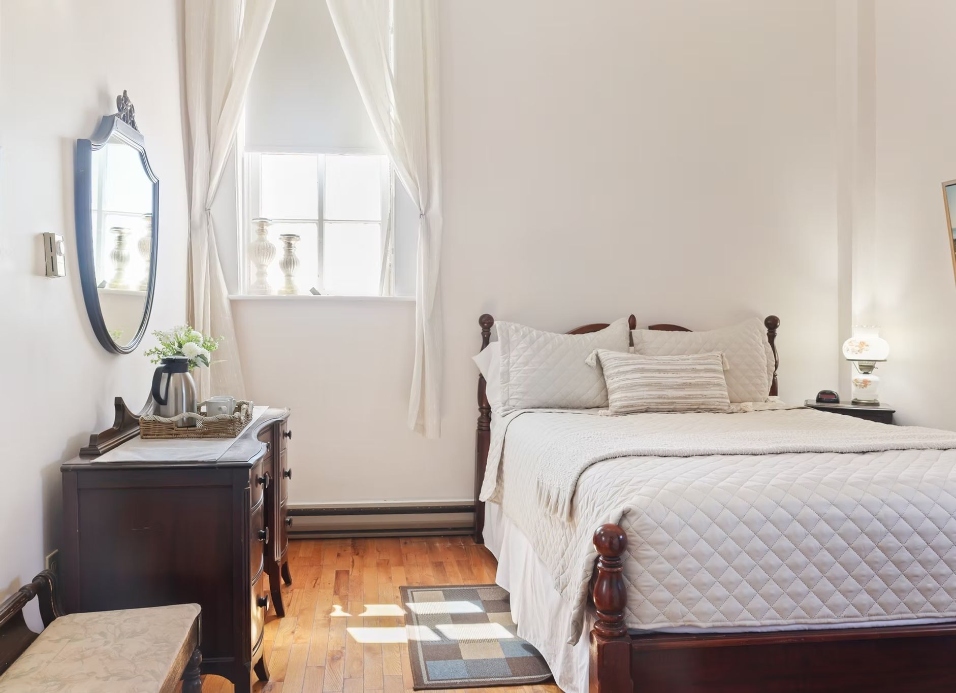 Kleine slaapkamer met een bed, bureau, spiegel en raam in zachte, neutrale tinten.