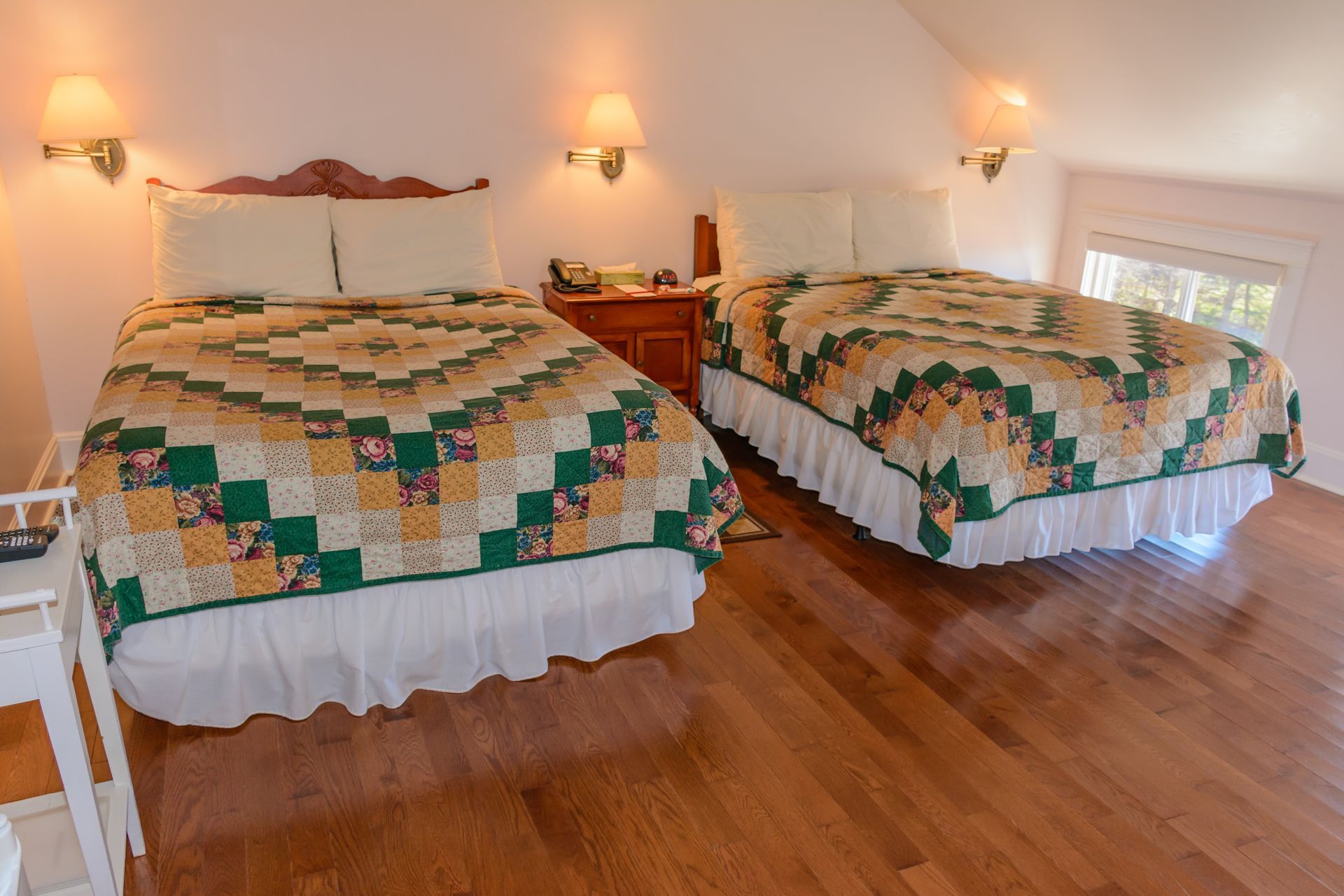 Lichte slaapkamer met twee eenpersoonsbedden, bedekt met groene, gele en witte dekens, op een houten vloer.