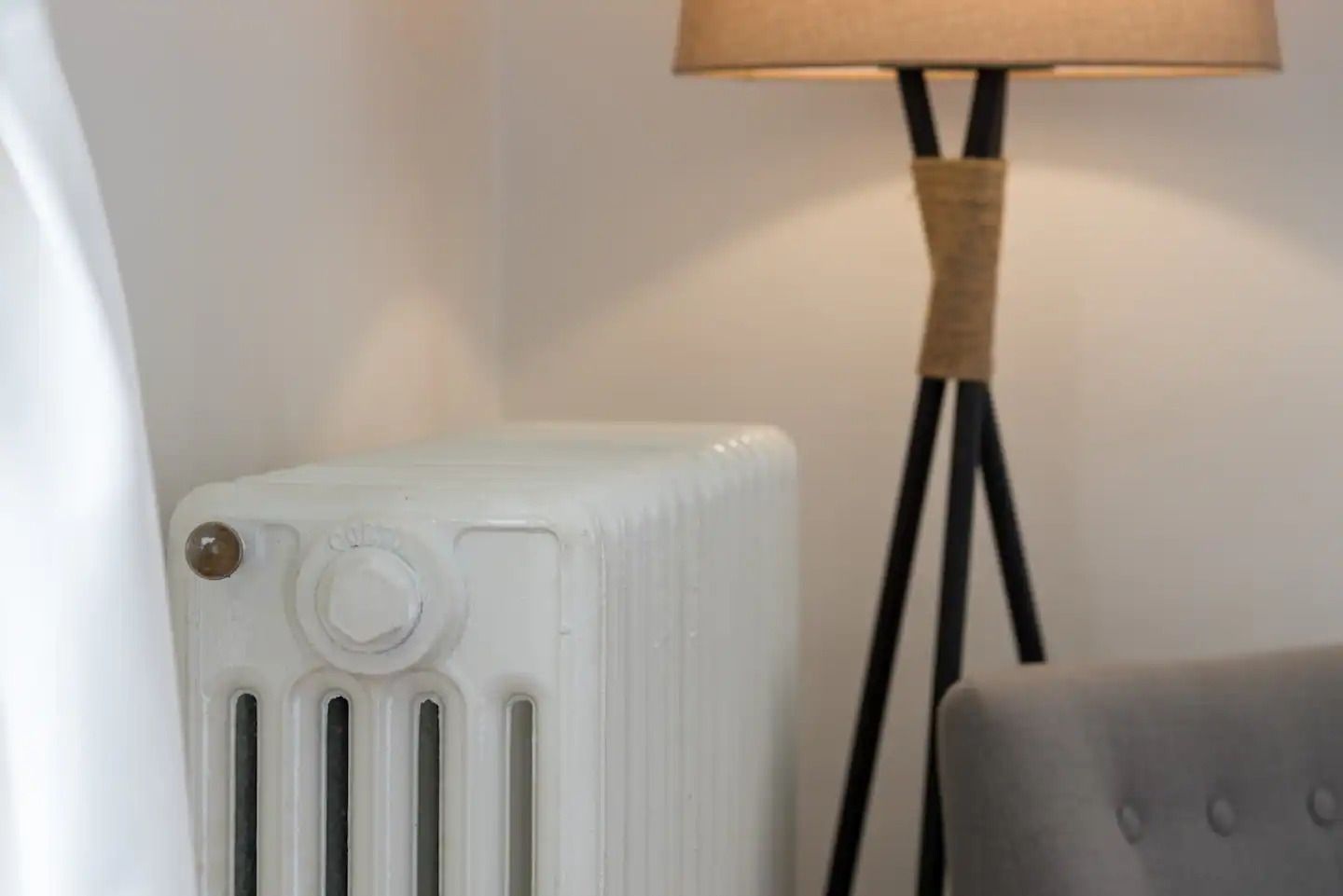 Witte radiator naast een beige staande lamp en een grijze bank in een gezellige kamer.