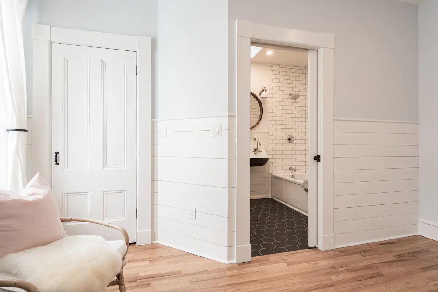 Lichte slaapkamer met witte lambrisering, open doorgang naar een betegelde badkamer en houten vloer.