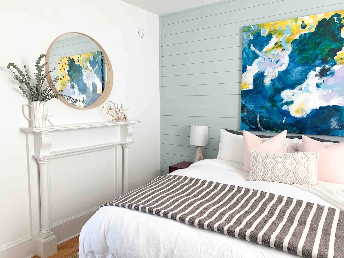 Lichte slaapkamer met wit bed, gestreepte deken, turquoise accentmuur en groot abstract schilderij met bloemenmotief.