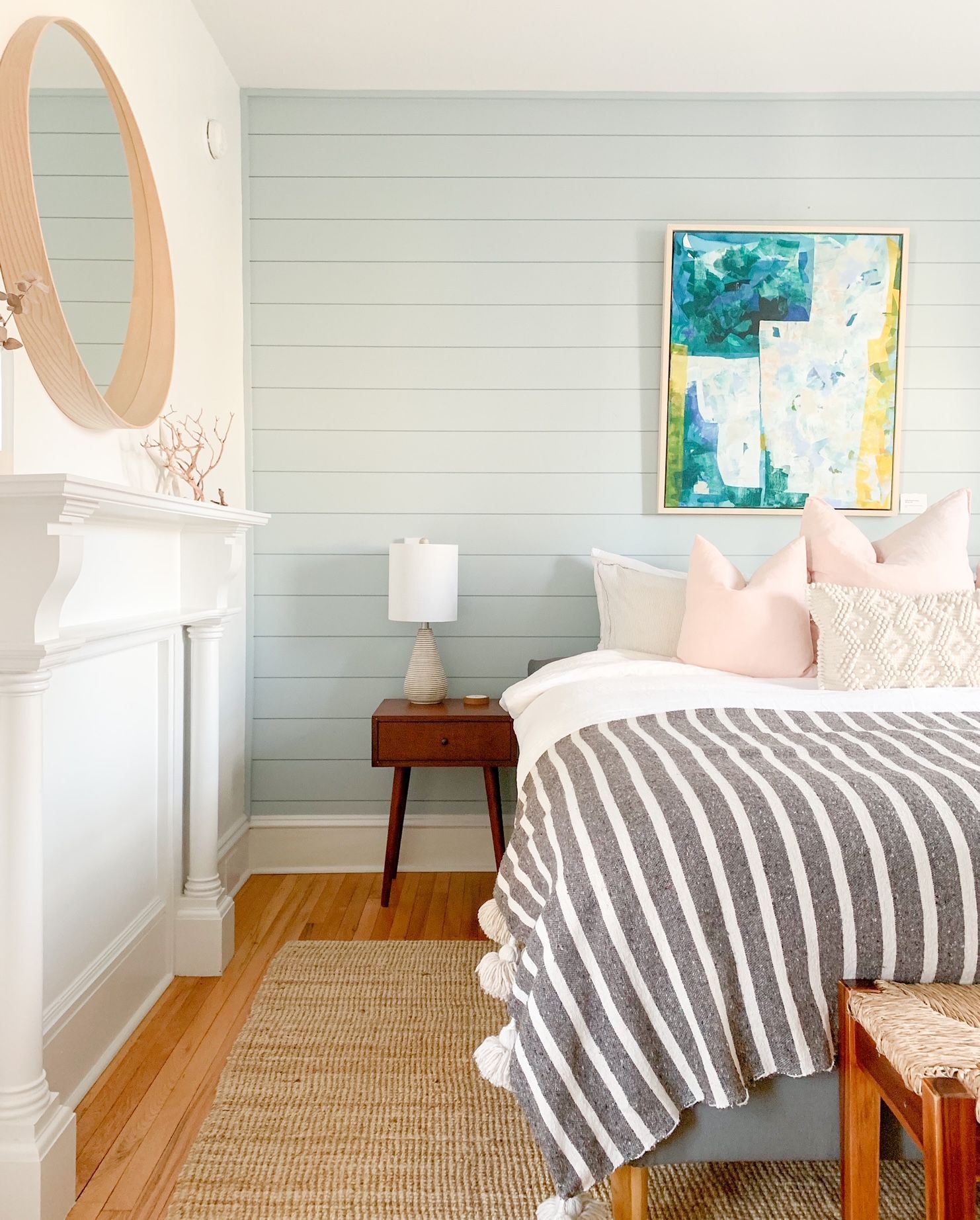 Lichte slaapkamer met witte muren, gestreepte sprei, nachtkastje en abstracte muurdecoratie.