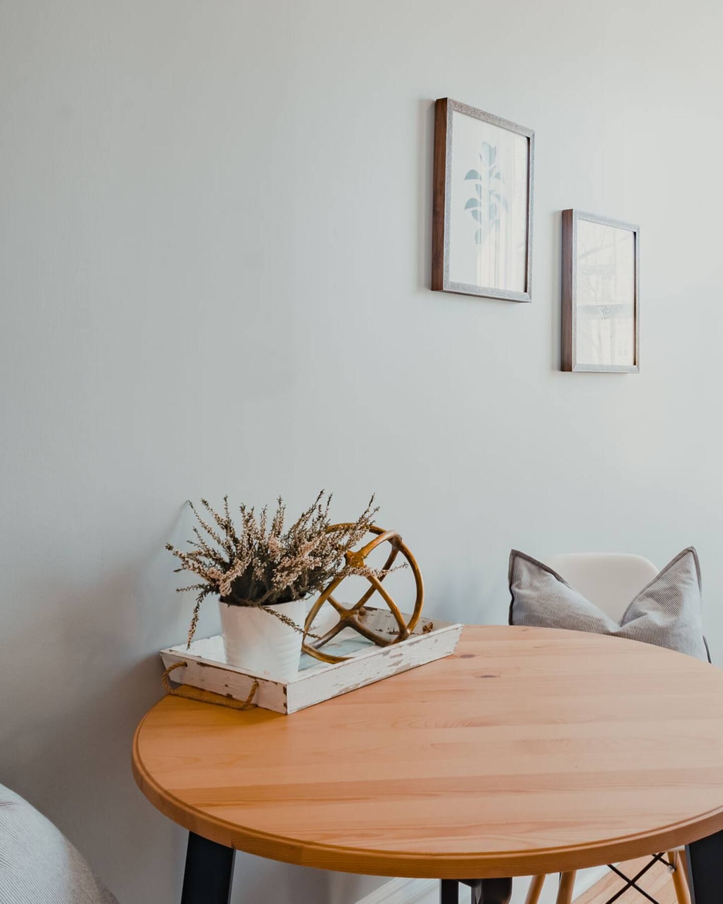 Minimalistische eethoek met ronde houten tafel, witte muurdecoratie en een decoratief dienblad als middelpunt.