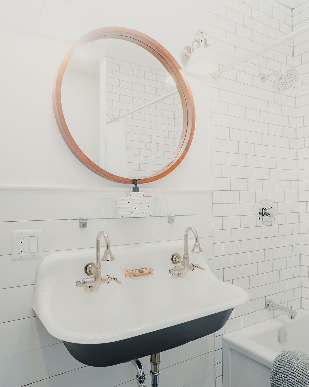Kleine witte wastafel in de badkamer met een ronde spiegel met koperen frame en een witte tegelwand.