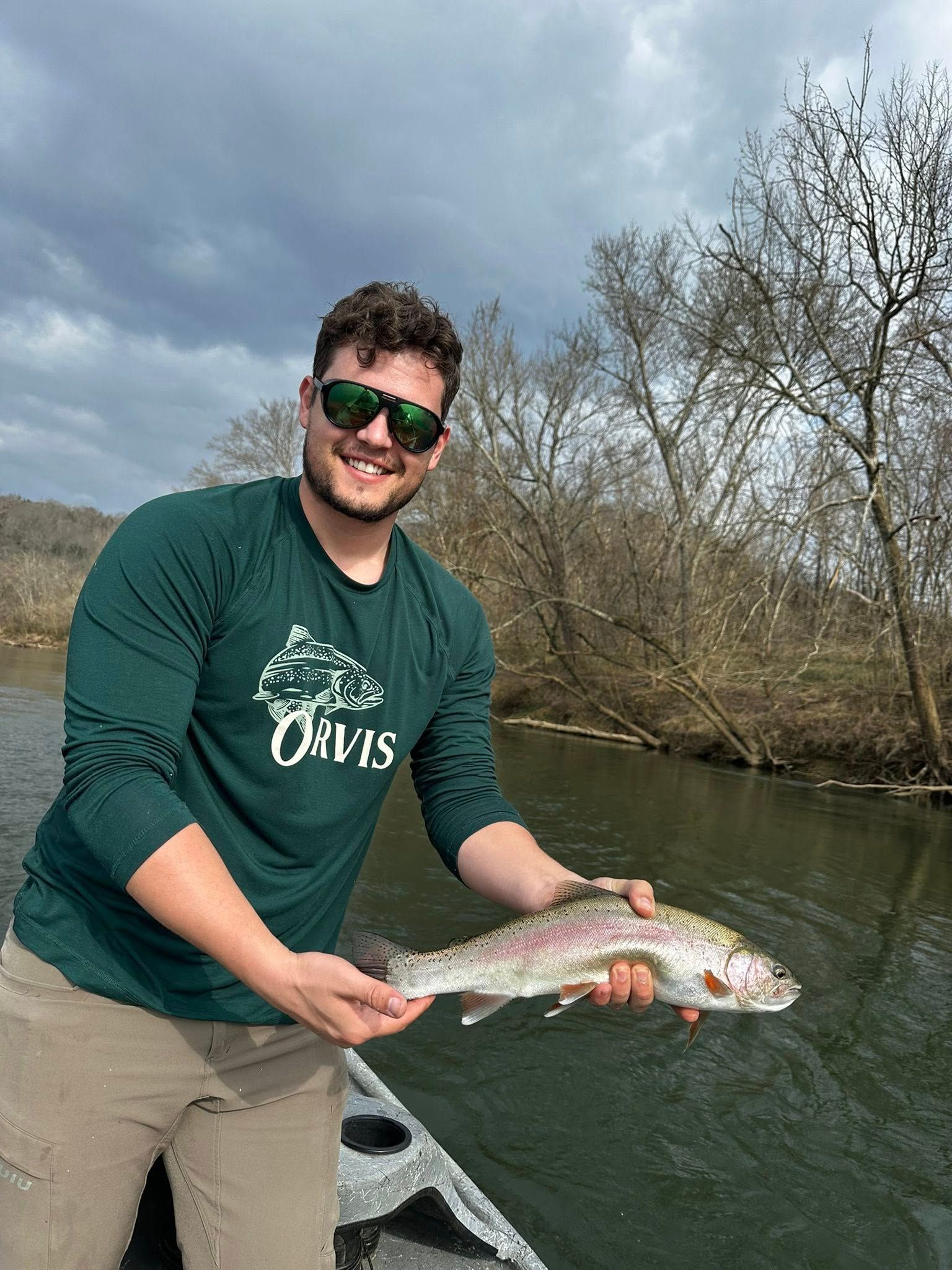 Rainbow trout held by angler in a boat, with visible pink stripe and speckled body.