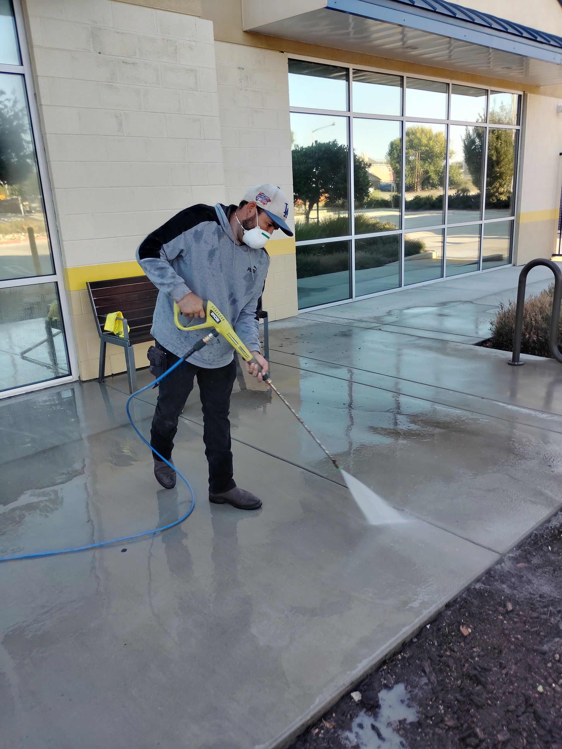 Worker in green clothes sanding a wooden floor with a power sander, wearing blue gloves.