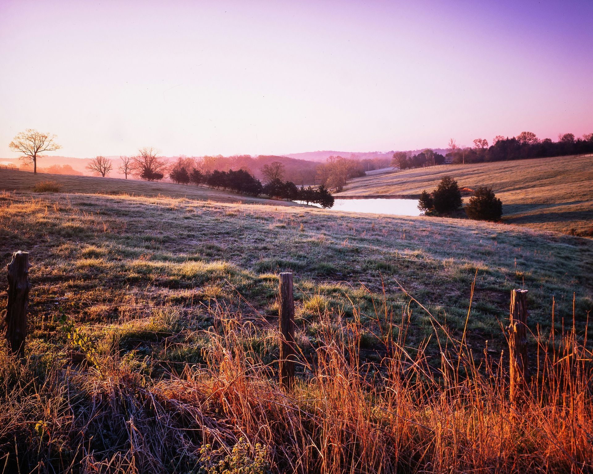 Sunrise over frosty rolling fields with a winding stream and pink sky