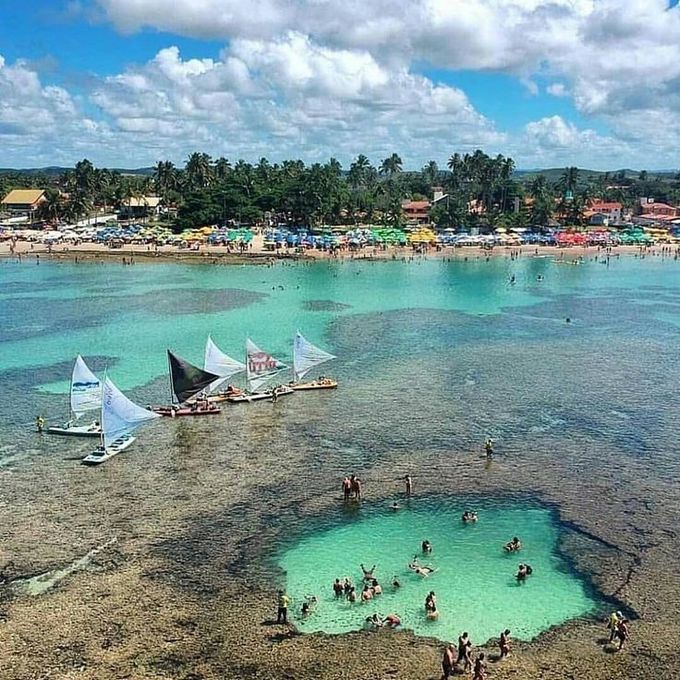 Um grupo de pessoas nada em uma pequena piscina no meio do oceano.