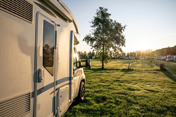 White camper van parked on a grassy field at sunset, with a tree and open landscape nearby