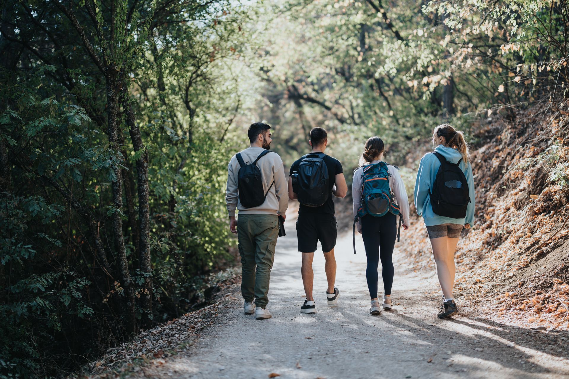 Four hikers with backpacks walking down a forest trail