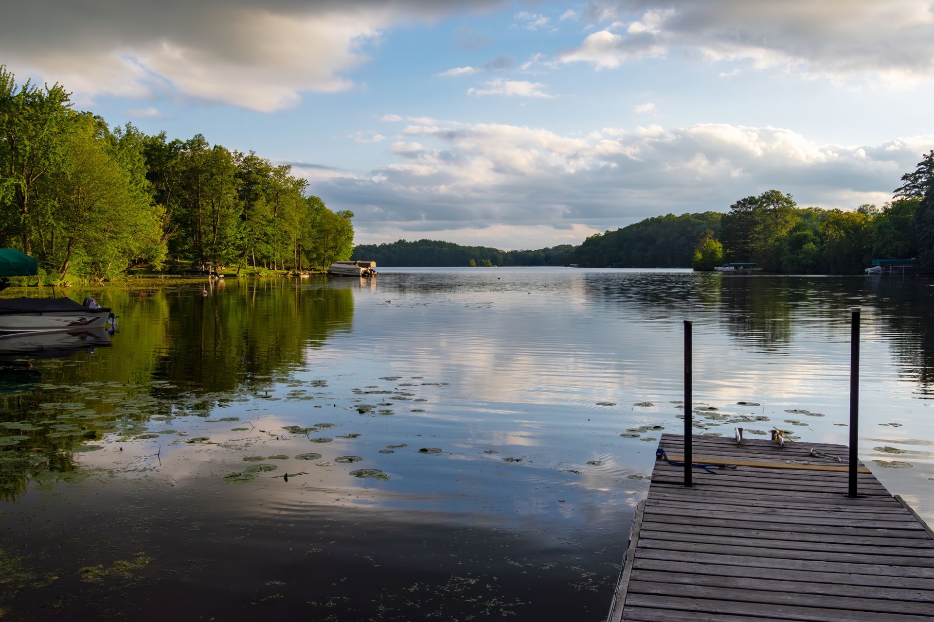 Calm lake with tree-lined shore, cloudy sky, and a dock in the foreground