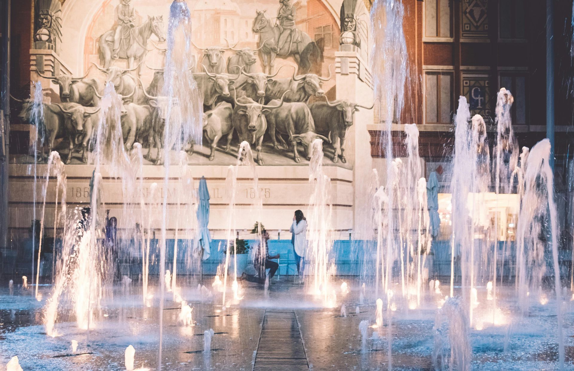 A woman is sitting on a bench in front of a fountain.