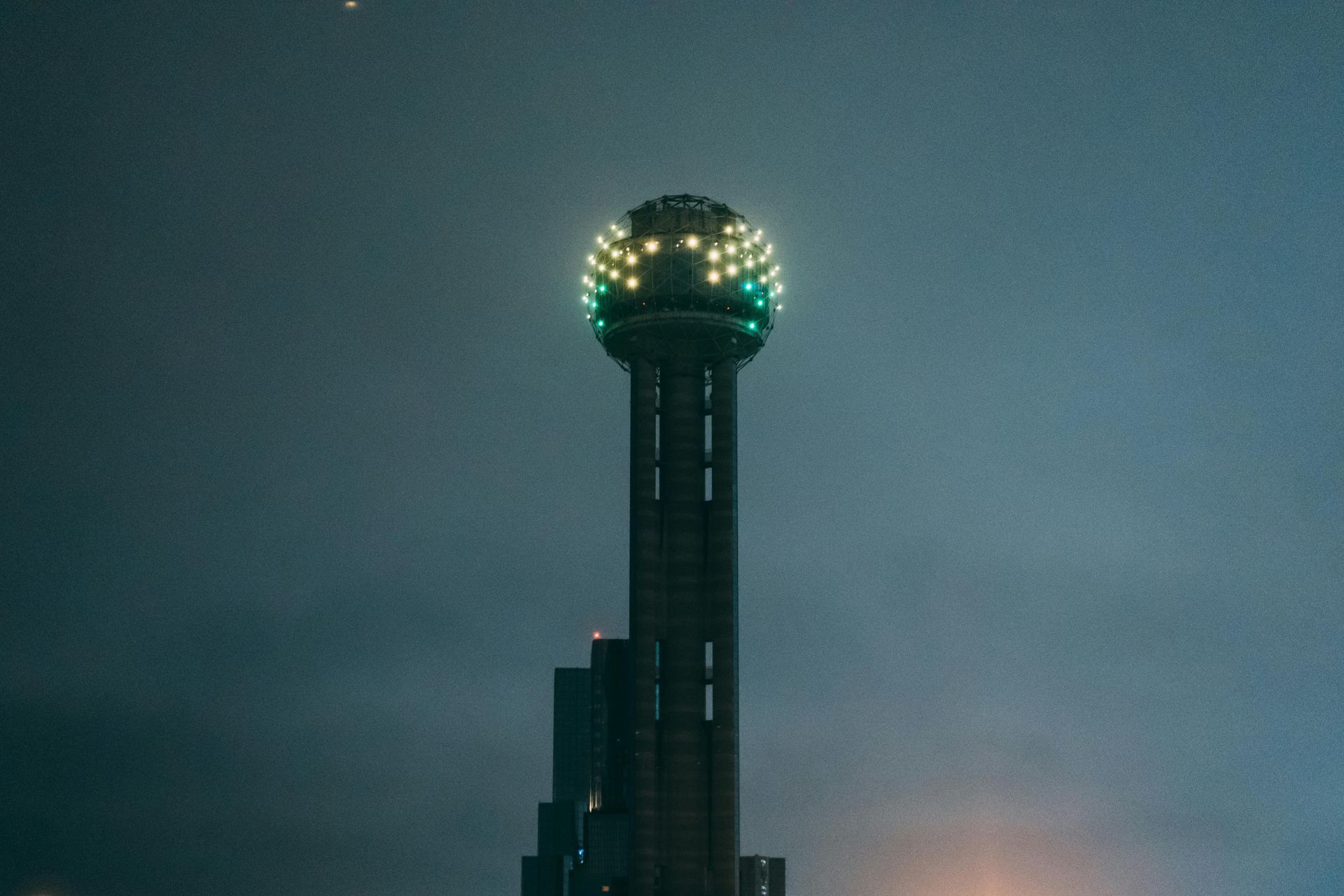 A tall tower with a green ball on top of it is lit up at night.