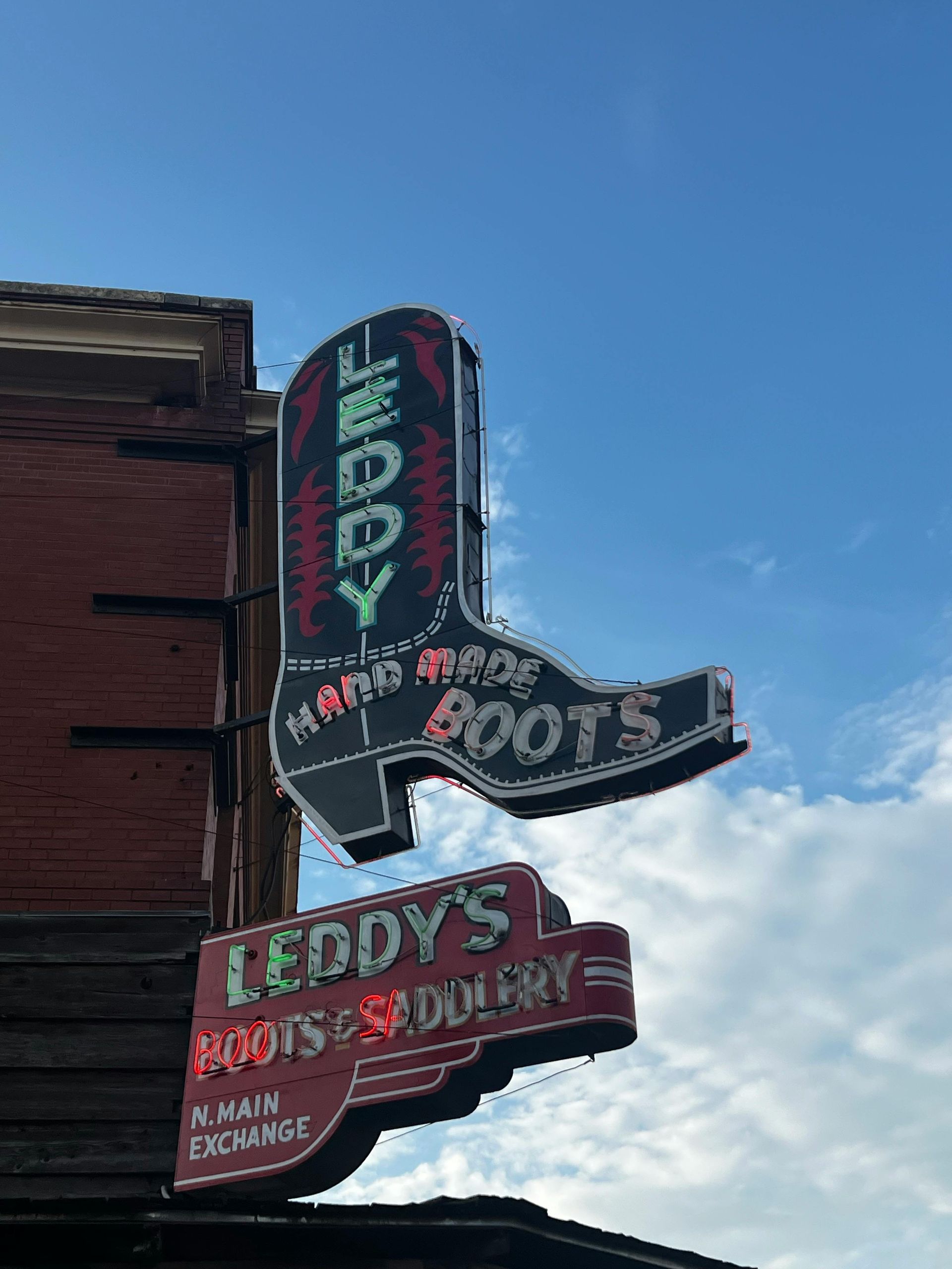 A neon sign in the shape of a cowboy boot is on the side of a building.