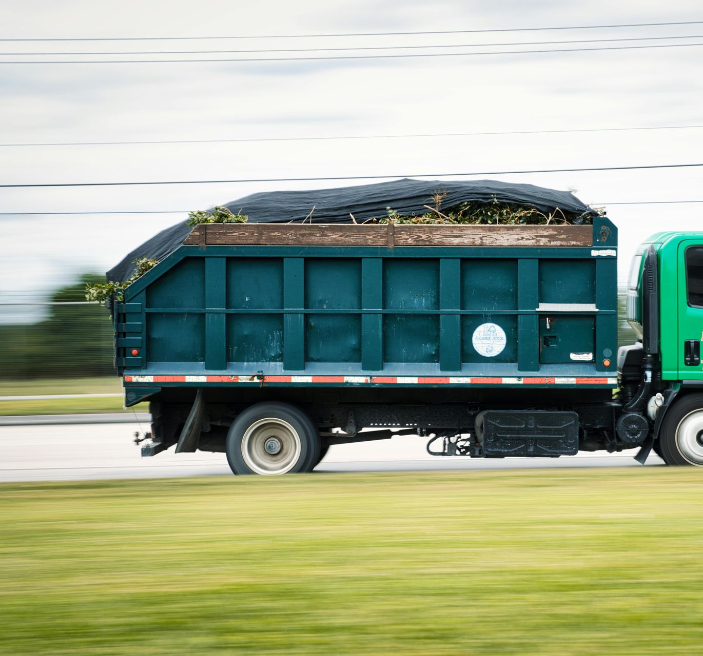 Green cargo truck loaded with plants driving on a road, blurred in motion
