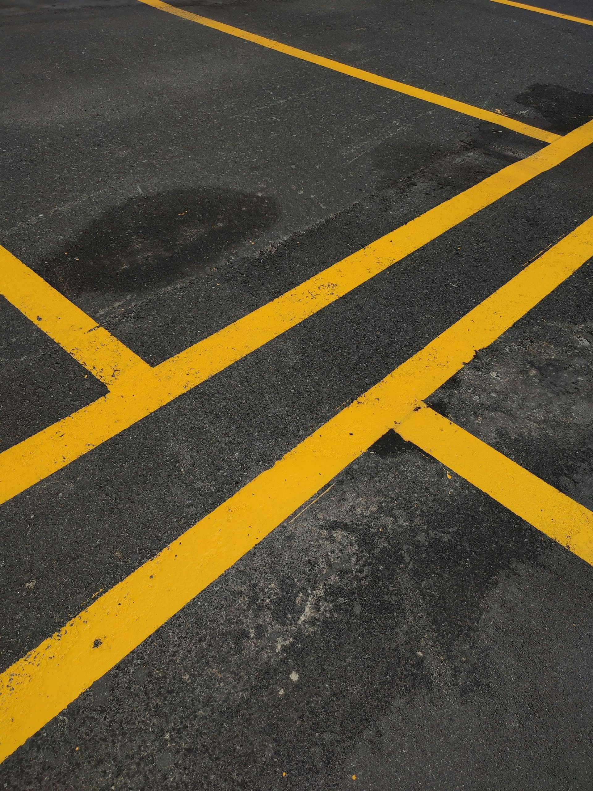 Yellow parking lot lines crossing on dark asphalt pavement.