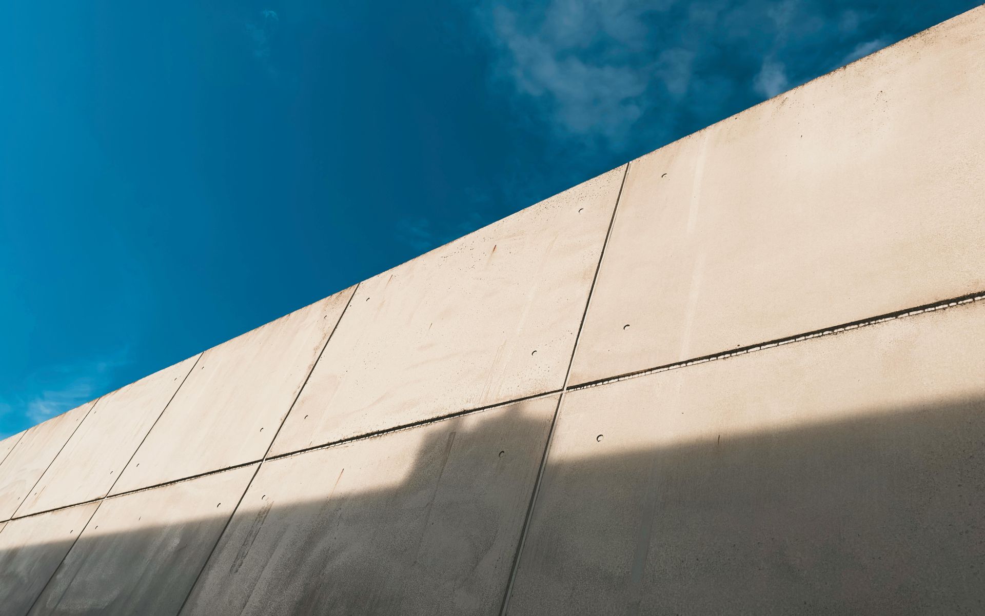 Blue sky above a beige concrete wall with a diagonal shadow across it