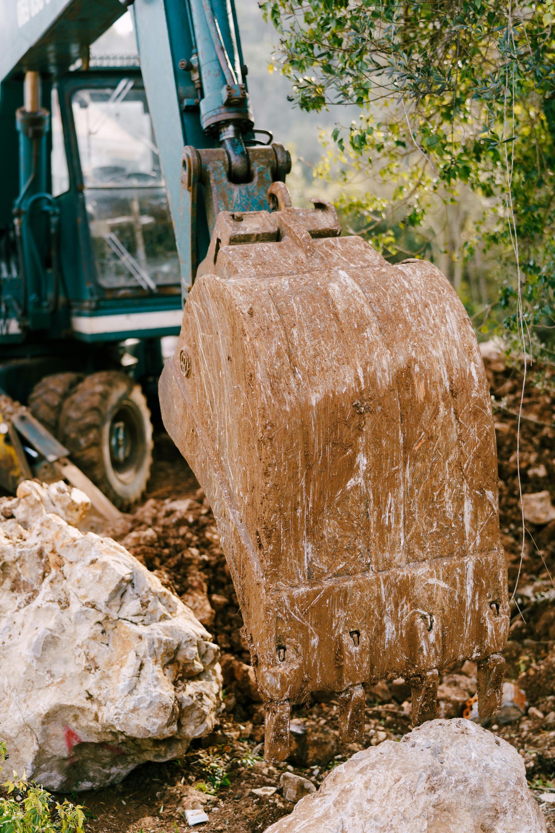 Excavator bucket pouring soil and gravel beside large rocks outdoors
