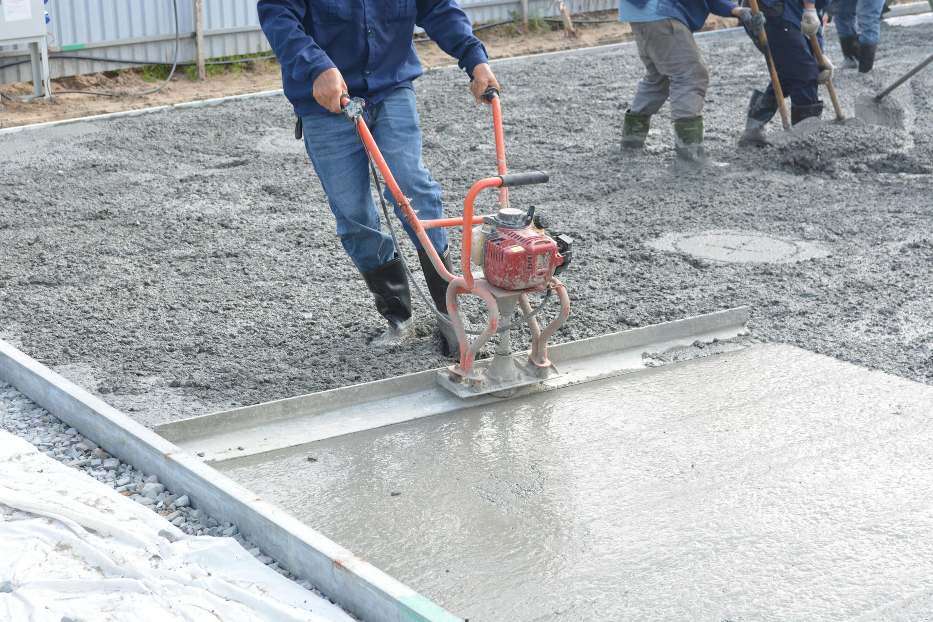 Workers using a concrete screed to smooth wet pavement at a construction site