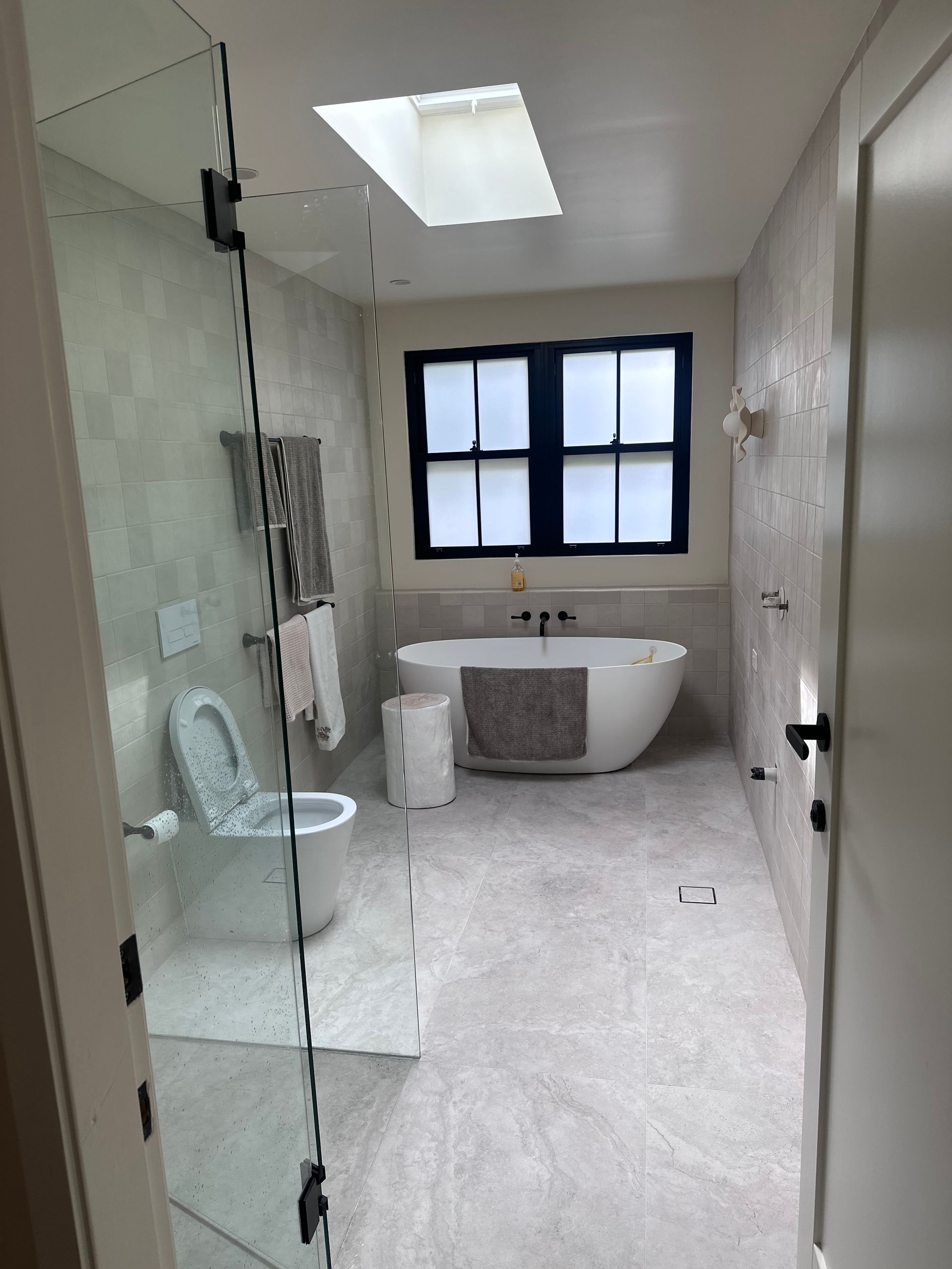 Modern bathroom with white walls, skylight, soaking tub, toilet, and glass shower door.