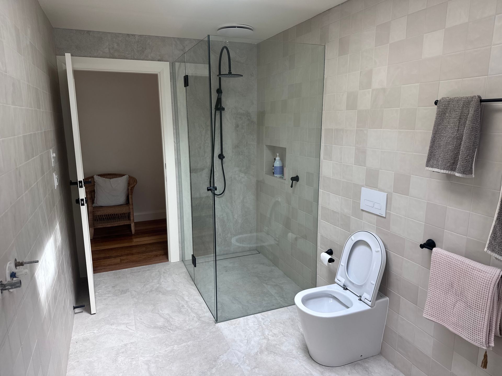 Modern bathroom with glass shower, toilet, and towel racks. Light gray tiled walls and flooring.