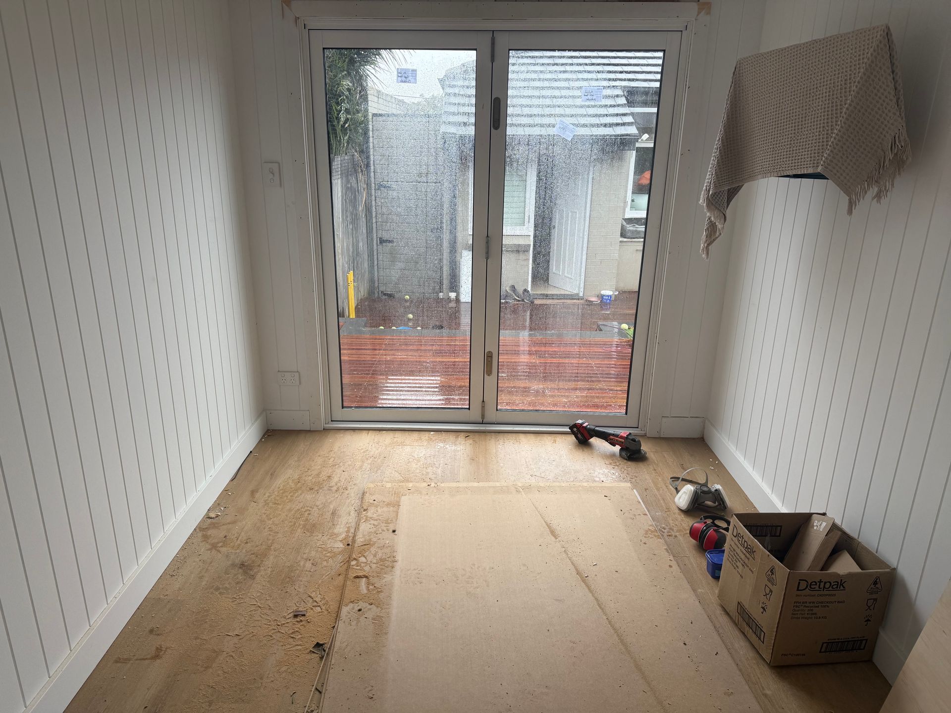 Interior room with wooden floor, white paneled walls, and a glass door leading to a back patio.