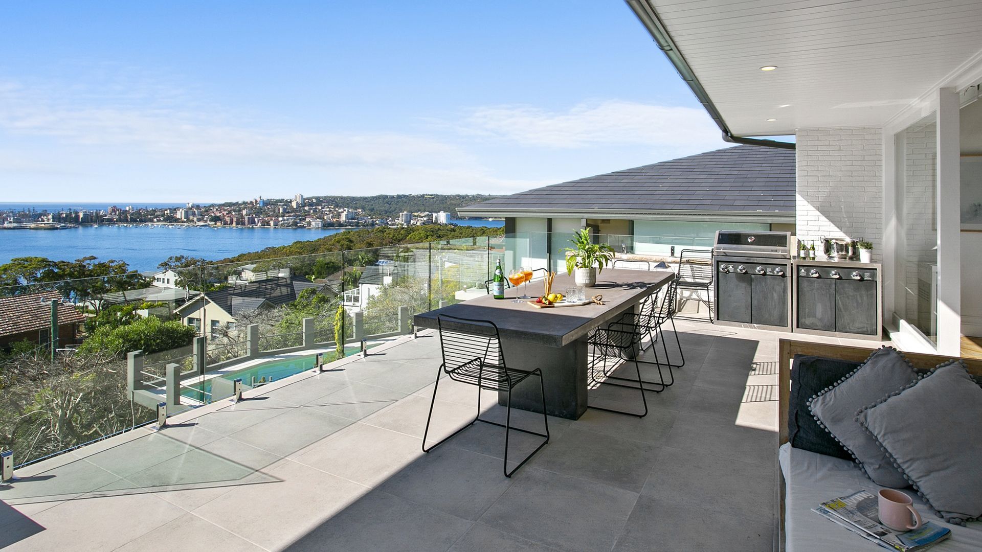 Outdoor patio with ocean view, table with food, seating area, glass railing.