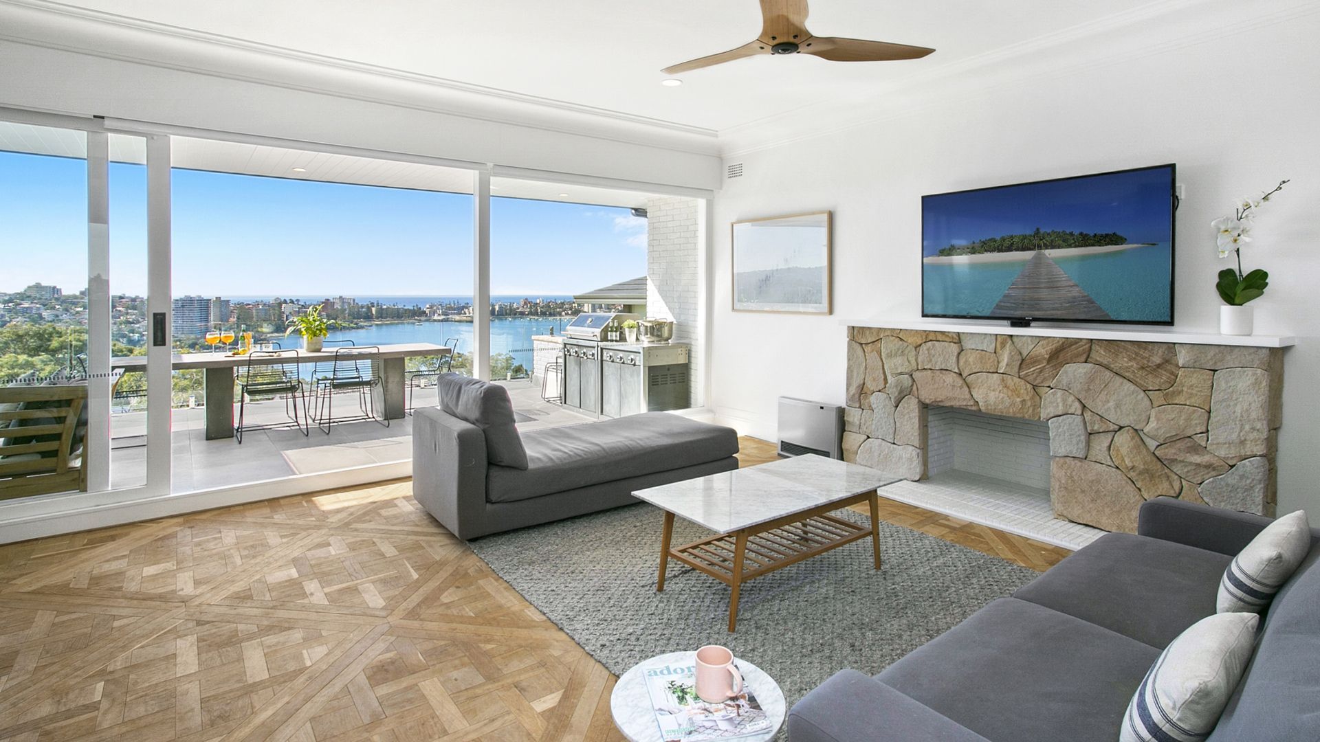 Living room with water view, gray sofa, stone fireplace, balcony.