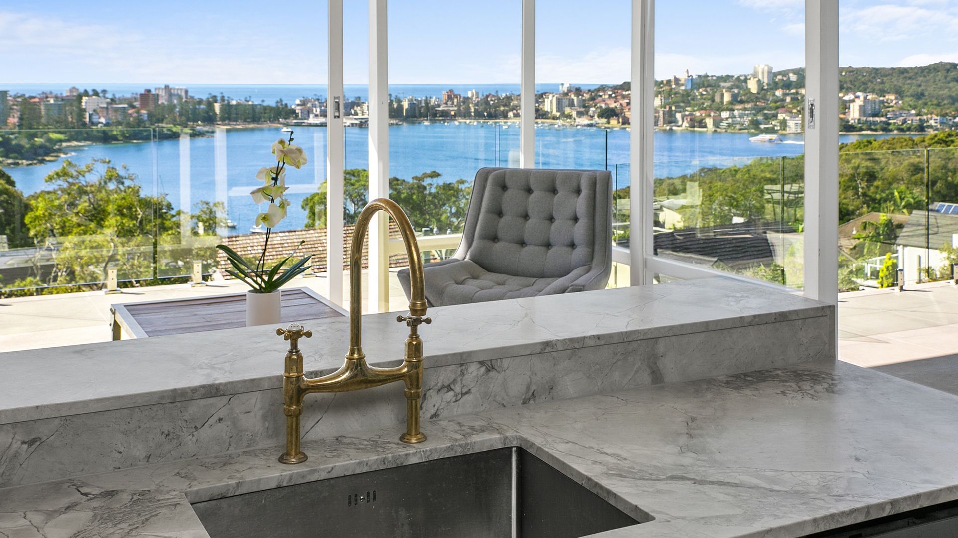 Kitchen with marble countertop, gold faucet, and view of water and city through large windows.