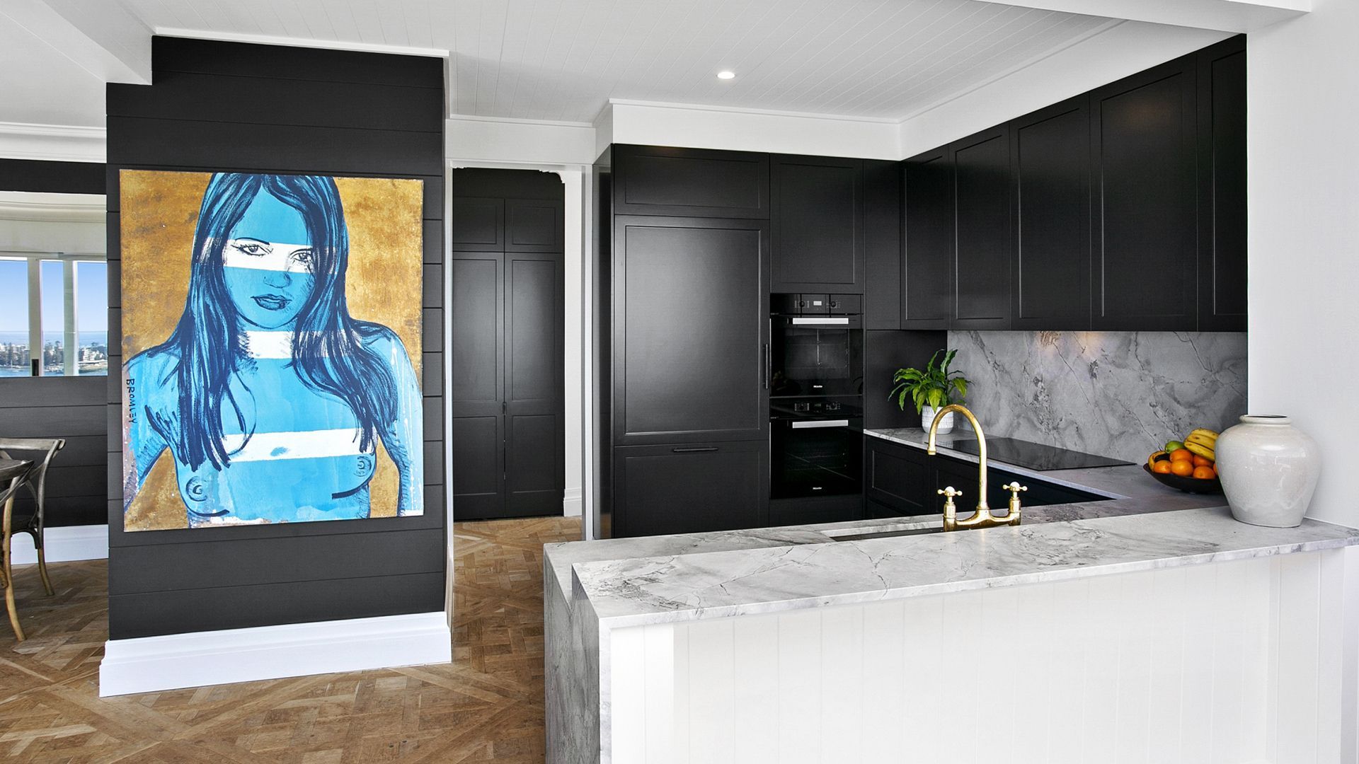 Modern kitchen with black cabinets, marble countertops, and vibrant artwork.
