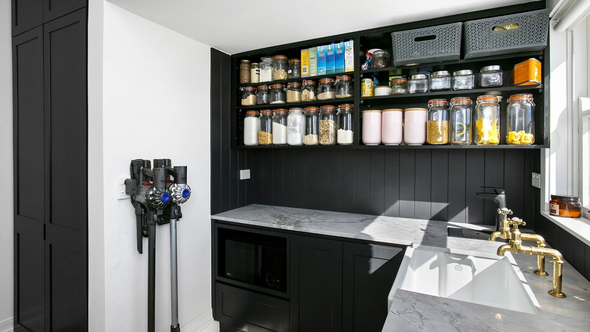 Black pantry with countertop, sink, and shelves filled with jars, plus a mounted vacuum cleaner.