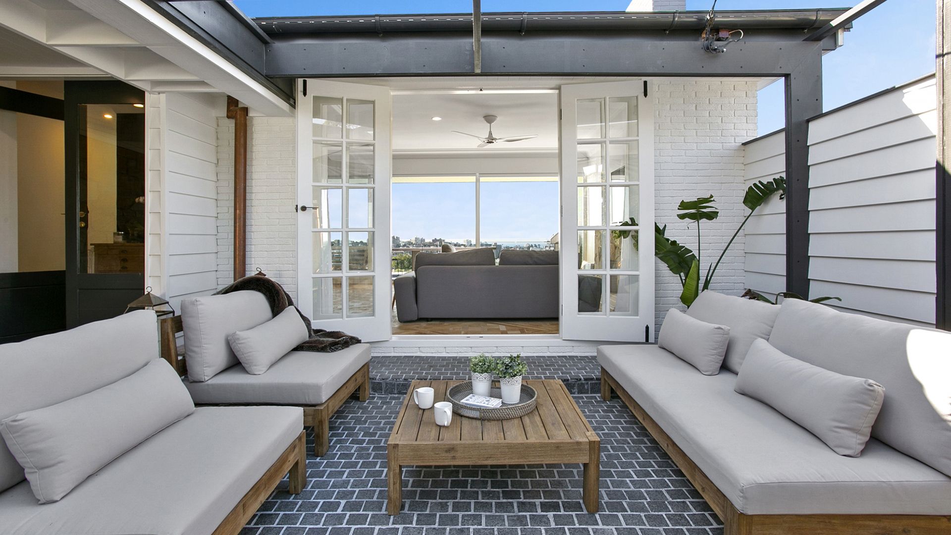 Patio with outdoor seating, wooden coffee table, and open doors to a living room with city views.