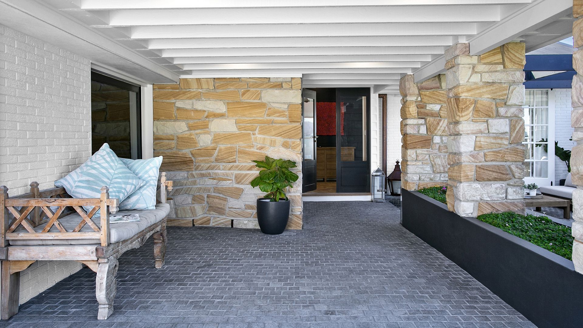 Stone porch with a wooden bench, black potted plant, and a dark front door.