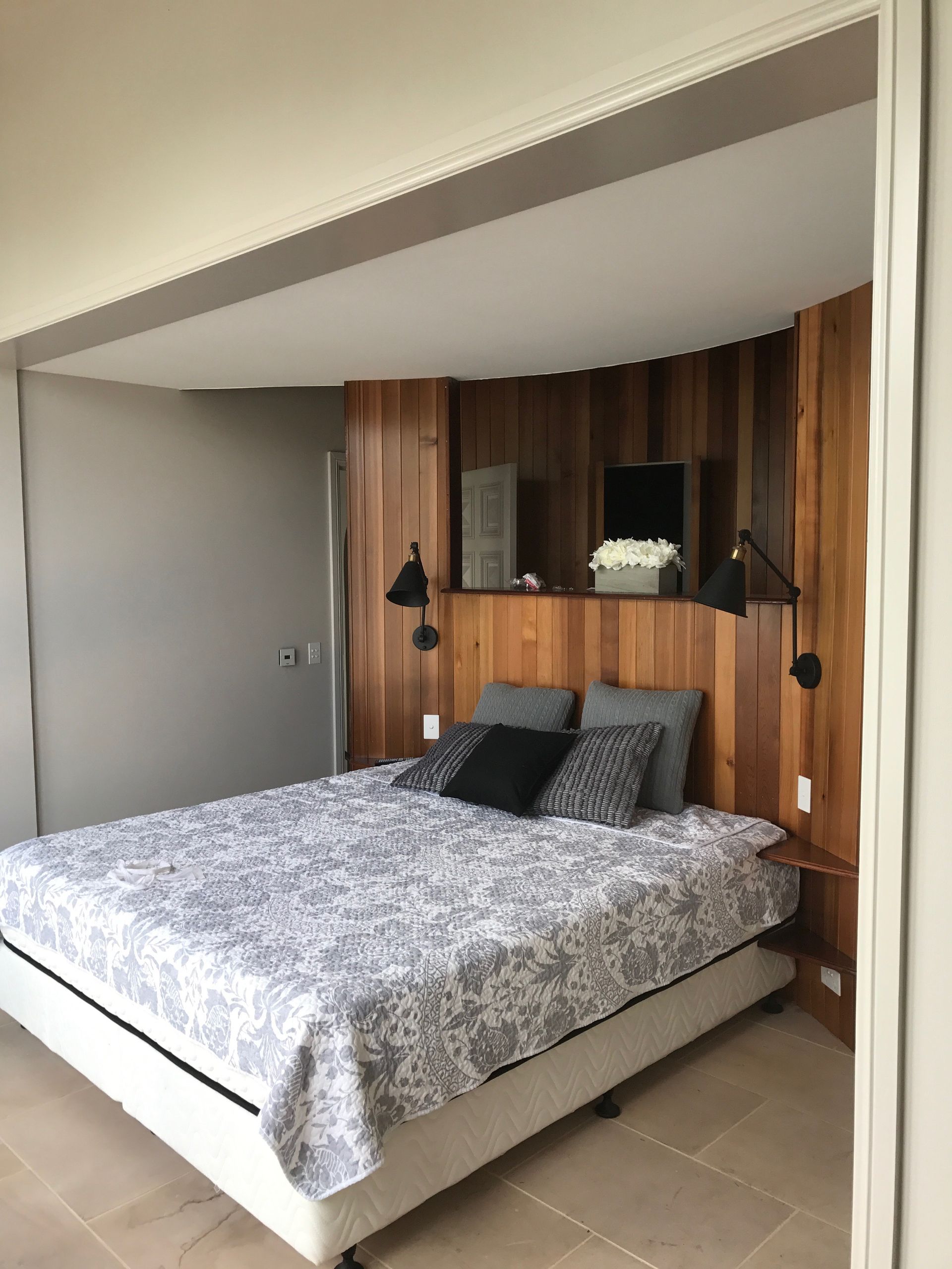 Bedroom with a bed, wooden headboard, and two black wall-mounted lamps.