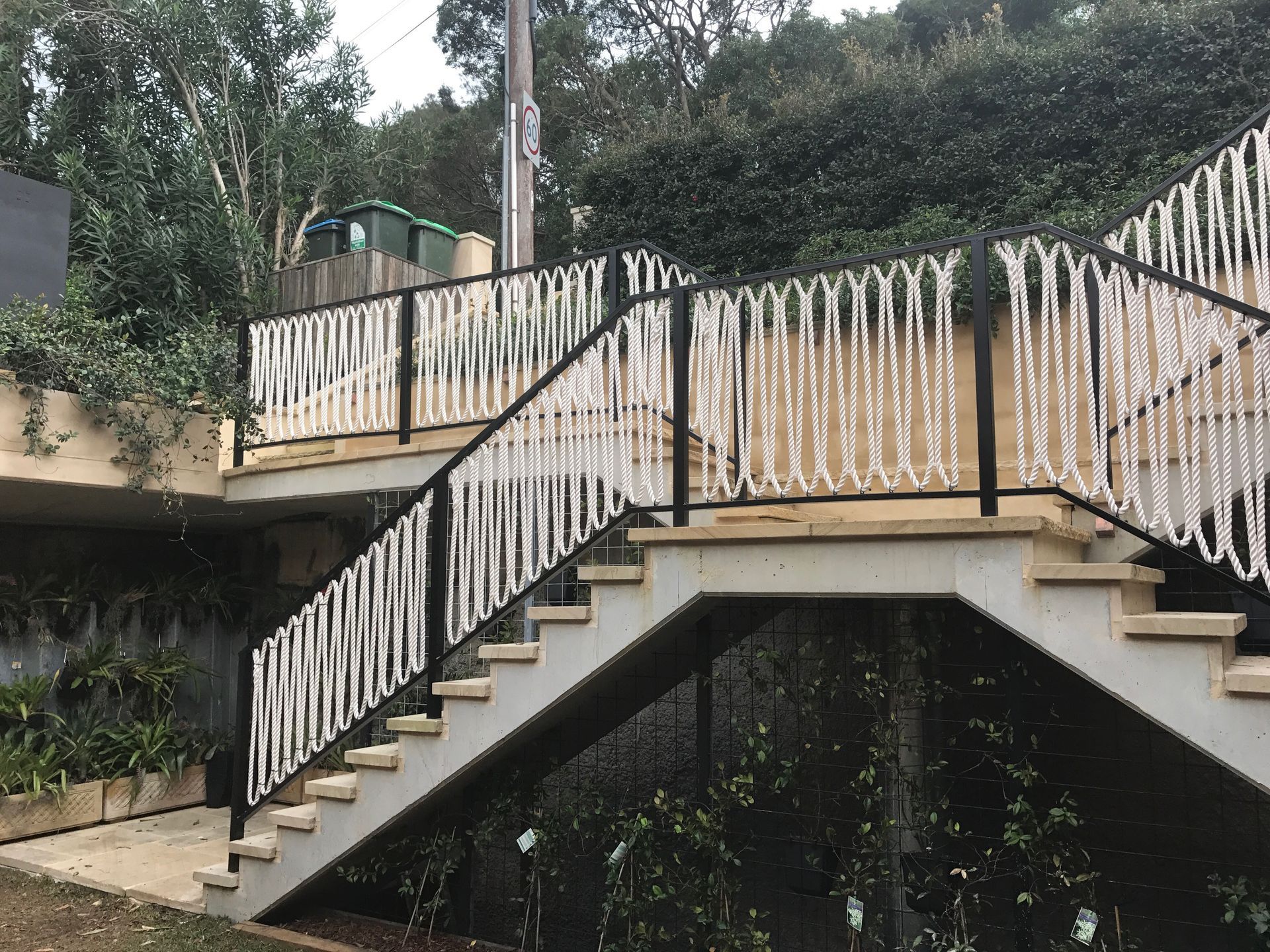 Outdoor concrete staircase with black railing and white rope details. Overlooking hillside greenery.