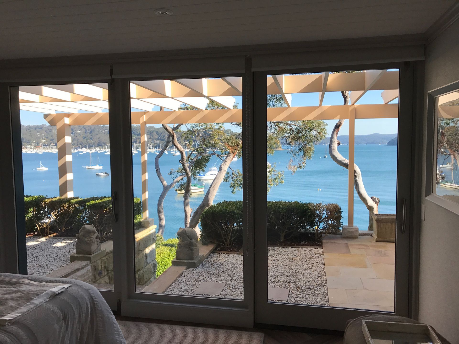 Bedroom with sliding glass doors overlooking a blue bay, trees, and white yachts.