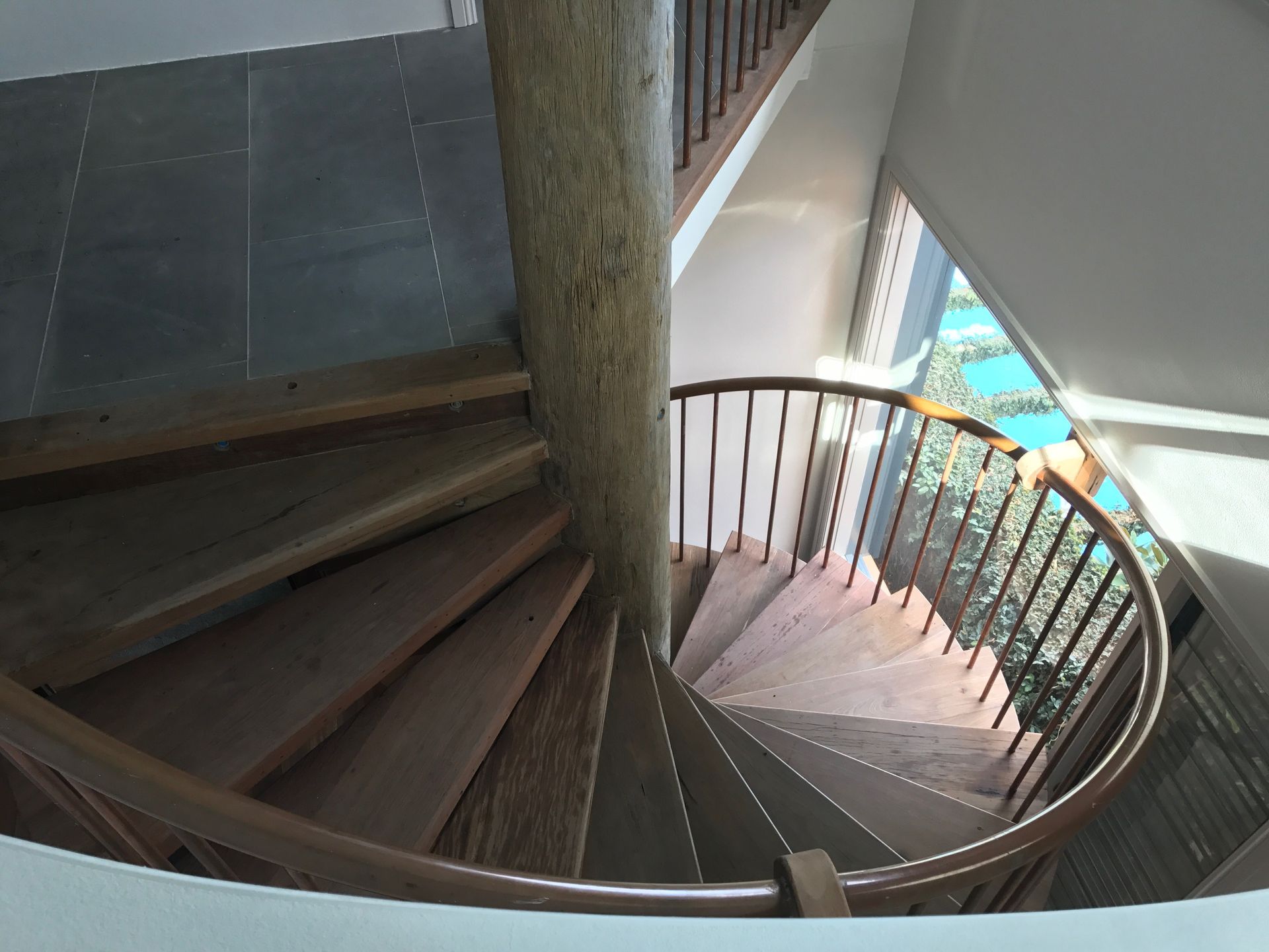 Spiral wooden staircase wraps around a central support beam. Sunlight streams through a window.