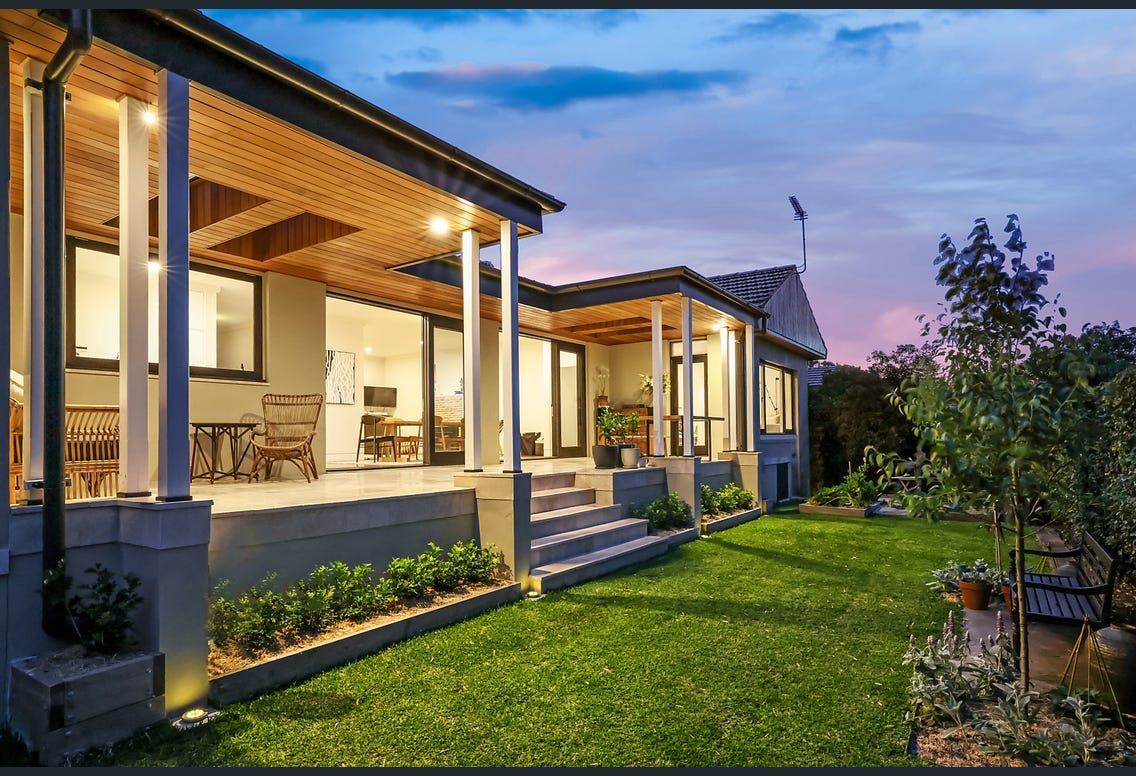 Exterior of a house at dusk with illuminated porch, grass lawn, and garden.