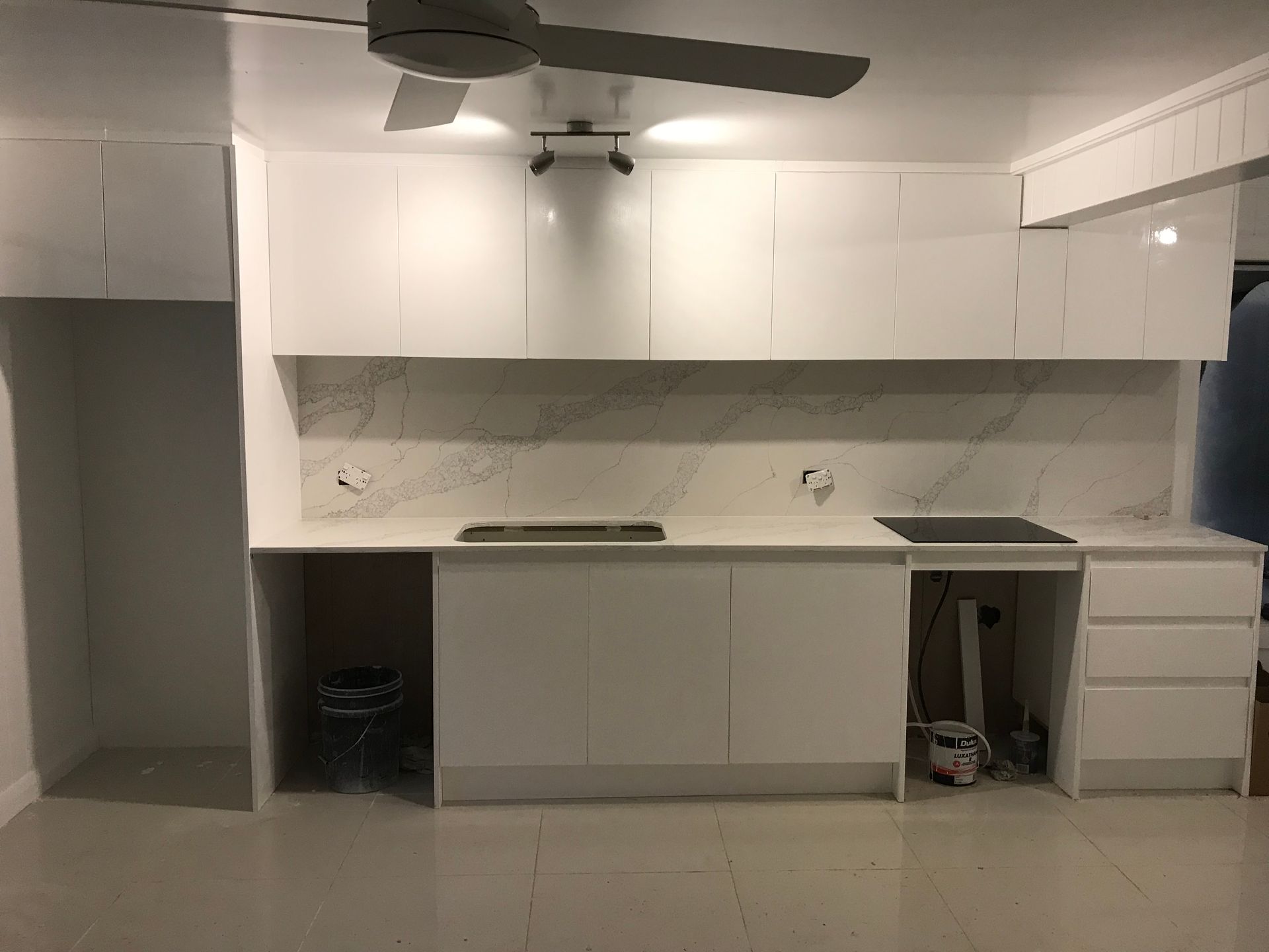 White kitchen with upper cabinets, countertops, and appliances against a marble backsplash.