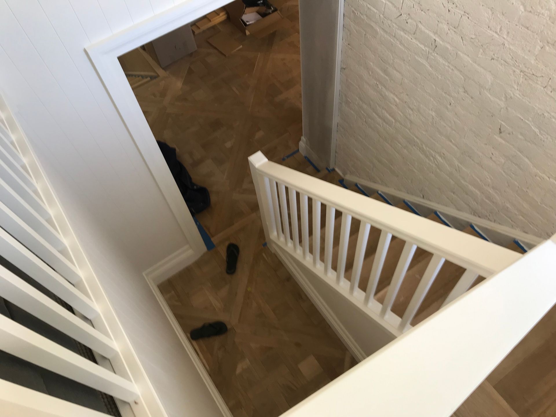 Staircase with white railing descending to a room with wood flooring, and a white brick wall.